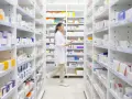 Farmaceutka w białym fartuchu idzie między regałami pełnymi leków, szukając amoksycyliny.