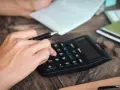 Ein getrennt lebender Ehemann macht Schulden. Er sitzt am Tisch und rechnet mit einem Taschenrechner.