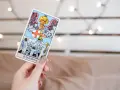 Una mano sostiene la carta de **el juicio tarot**, mostrando un ángel con trompeta y personas resucitando.
