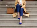 Elegancka stylizacja: beżowy płaszcz, jeansy i buty w kolorze habrowym. Obok torebka w odcieniu karmelu.