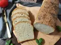 Świeżo upieczony chleb pszenny z makiem, pokrojony w kromki, obok pomidor i złoty nóż.