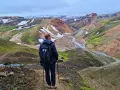 Un randonneur admire le paysage coloré de Landmannalaugar, avec ses montagnes aux teintes ocre, vertes et blanches.