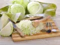 Przygotowanie kiszonej kapusty: ile soli na 10kg? Na desce poszatkowana kapusta, nóż, tłuczek, kminek, pieprz i sól.