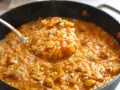 Cuchara llena de cremoso arroz con pollo de la abuela, humeante y con trozos de pollo y champiñones.