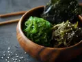 Trzy rodzaje jadalnych wodorostów: zielone wakame, ciemne kombu i sałatka z wodorostów z sezamem, w drewnianej misce.