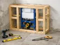 Cadre en bois pour un wc suspendu sur mur non porteur, avec réservoir et tuyauterie visibles. Outils de bricolage au sol.