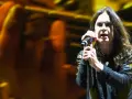 Ozzy Osbourne śpiewa do mikrofonu na koncercie, z rozmytym tłem w kolorach żółci i pomarańczy.