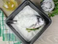 Dorada a la sal lista para hornear, con hierbas frescas y aceite de oliva al lado.