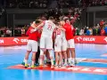 Drużyna piłkarzy ręcznych w białych strojach z czerwonymi elementami tworzy zgraną grupę na boisku.