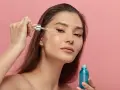 Kobieta aplikuje serum z retinyl palmitate na skórę pod okiem. Błękitna buteleczka kosmetyku w dłoni.