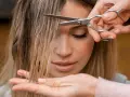 Manos cortando el flequillo de una mujer. Un momento perfecto para saber cuando es mejor cortarse el pelo y renovar tu look.