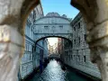 Il Ponte dei Sospiri a Venezia, visto da un'arcata, con gondole sull'acqua e un cielo azzurro.