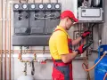 Instalator wykonuje próbę szczelności instalacji gazowej powietrzem, używając detektora. W tle widoczny kocioł i manometry.