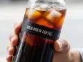 Dłoń trzyma butelkę z orzeźwiającym cold brew coffee, pełną kostek lodu. Idealna kawa do cold brew na upalne dni.