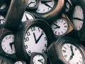 Stos starych zegarów, niektóre z rzymskimi cyframi, inne z arabskimi.