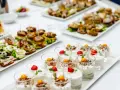 Varietà di antipasti freddi per buffet: mini hamburger, tartine con uova e salumi, e dolcetti in bicchiere con frutta e yogurt.