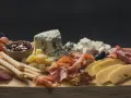 Apetyczna taca serów: pleśniowy, żółty, biały, wędliny, winogrona, oliwki, orzechy i dżem.