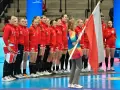 Drużyna piłki ręcznej kobiet Polski w czerwonych strojach stoi w rzędzie, trzymając polską flagę.