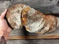 Ein rustikales wurzelbrot mit sauerteig, bestäubt mit Mehl, liegt auf einem Holzbrett.