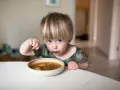Mały chłopiec z blond grzywką zajada pyszną zupę. To idealne zupy dla dzieci, które rozgrzewają i dodają energii.