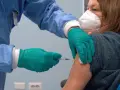 Osoba w niebieskim fartuchu i zielonych rękawiczkach podaje zastrzyk. Kobieta w masce KN95 otrzymuje trzecią dawkę szczepionki.