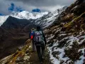 Dwóch turystów z plecakami wędruje ścieżką u podnóża ośnieżonych gór, przypominających krajobraz Mount Kenya.