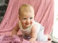 Ein lächelndes Baby krabbelt auf einer rosafarbenen Decke. Es ist etwa 26 Wochen alt und erlebt gerade einen Entwicklungsschub.