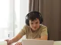 Chłopiec w słuchawkach uczy się zdalnie, notując. Dopełnienie odpowiada na pytania: kogo? czego? komu? czemu? kogo? co? czym? kim? o kim? o czym?