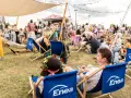 Ludzie odpoczywają na leżakach z logo Enea podczas festiwalu. W tle scena i tłum.