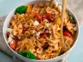 Ein köstlicher, sommerlicher Nudelsalat mit Farfalle, Tomaten, Feta und Basilikum, serviert in einer weißen Schüssel mit Holzutensilien.