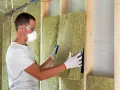 Operaio con mascherina e occhiali installa pannelli isolanti, mostrando il **coibentazione significato** per un ambiente efficiente.