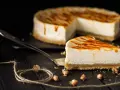 Una fetta di cheesecake senza panna, con glassa caramellata, su un piatto da portata, con la torta intera sullo sfondo.