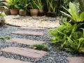 Schrittplatten führen durch einen Kiesgarten. Ein Steingarten anlegen wird hier mit Farnen und Gräsern umgesetzt.