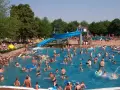 Ein belebtes Freibad in Goslar mit vielen Menschen, die im Wasser planschen und die blaue Wasserrutsche genießen.