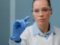 Naukowczyni w okularach ochronnych bada próbkę pod mikroskopem. Czy diagnostyka robi badania na NFZ?