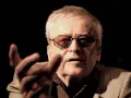 Jerzy Jarocki w okularach, z gestem dłoni, w ciemnym tle.