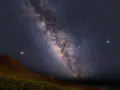 Paisaje nocturno en una reserva starlight, con la Vía Láctea cruzando el cielo estrellado sobre una colina y vegetación.