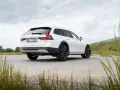 Białe Volvo Cross Country na tle pochmurnego nieba i zielonych wzgórz.