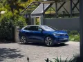 Niebieski Volkswagen ID.4 ładuje się przy domu, otoczony zielenią.