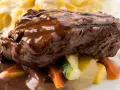 Succulento brasato di manzo nappato con salsa scura, servito su verdure miste e accompagnato da pasta.