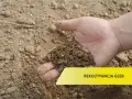 Dłoń trzyma żyzną ziemię, symbolizującą przywrócenie gruntu do produkcji rolnej. Rekultywacja gleb to klucz do urodzaju.