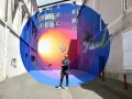 Un artiste street art français pose devant sa fresque colorée d'une fillette et d'un lapin flottant dans un tunnel psychédélique.