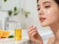 Une goutte d'huile à la vitamine C sur la joue d'une femme, à côté d'une bouteille et d'oranges.