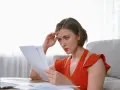Zmartwiona kobieta z ręką na czole czyta dokumenty, obawiając się, że padła ofiarą ultimo oszuści.