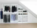 Einbauschrank selber bauen: Weißer Schrank mit Kleiderstangen, Schubladen und Schuhfächern unter einer Dachschräge.