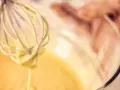 Frusta da cucina che raccoglie una densa pastella per fritti, pronta per creare delizie croccanti.