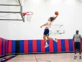 Un joueur de basket-ball en plein saut, ballon en main, effectue un exercice de pliométrie. Un autre joueur observe.
