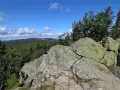 Kamienne formacje na rozdrożu izerskim, porośnięte mchem, z widokiem na gęsty las i błękitne niebo z chmurami.