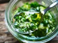 Łyżka z aromatycznym, zielonym sosem chimichurri, pełnym ziół i czosnku, zanurzona w słoiku.