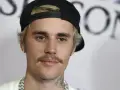 Justin Bieber con un gorra negra y un bigote herradura, luciendo una cadena plateada.